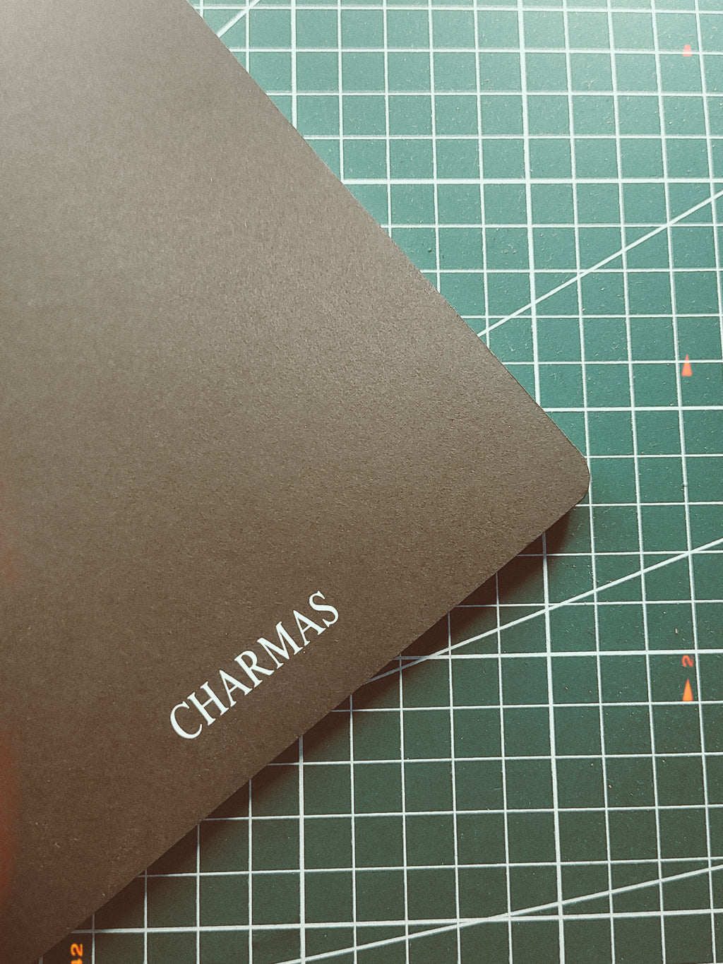 Brown notebook with 'CHARMAS' branding on a green cutting mat.