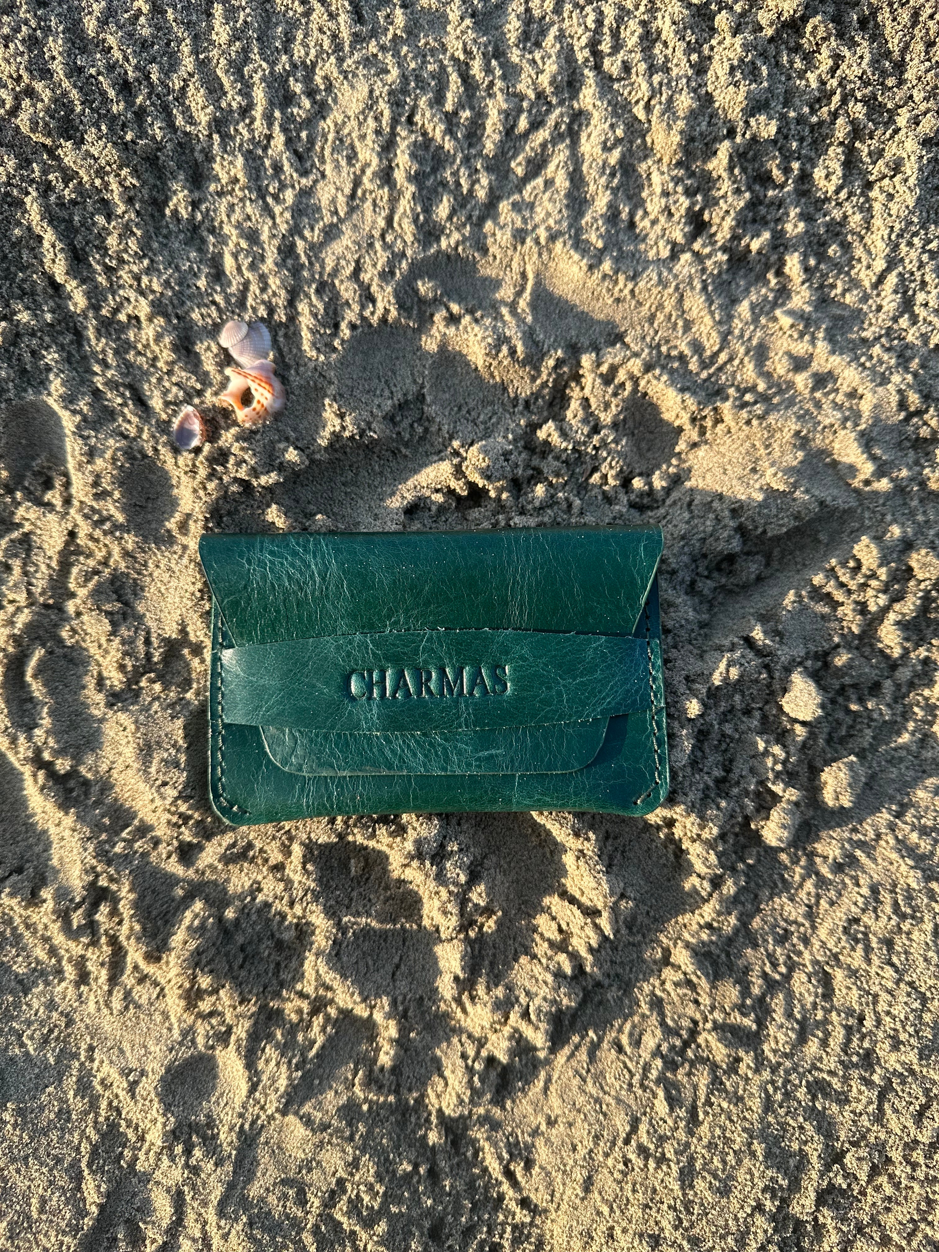 Green leather wallet with 'Charmas' branding on sandy ground