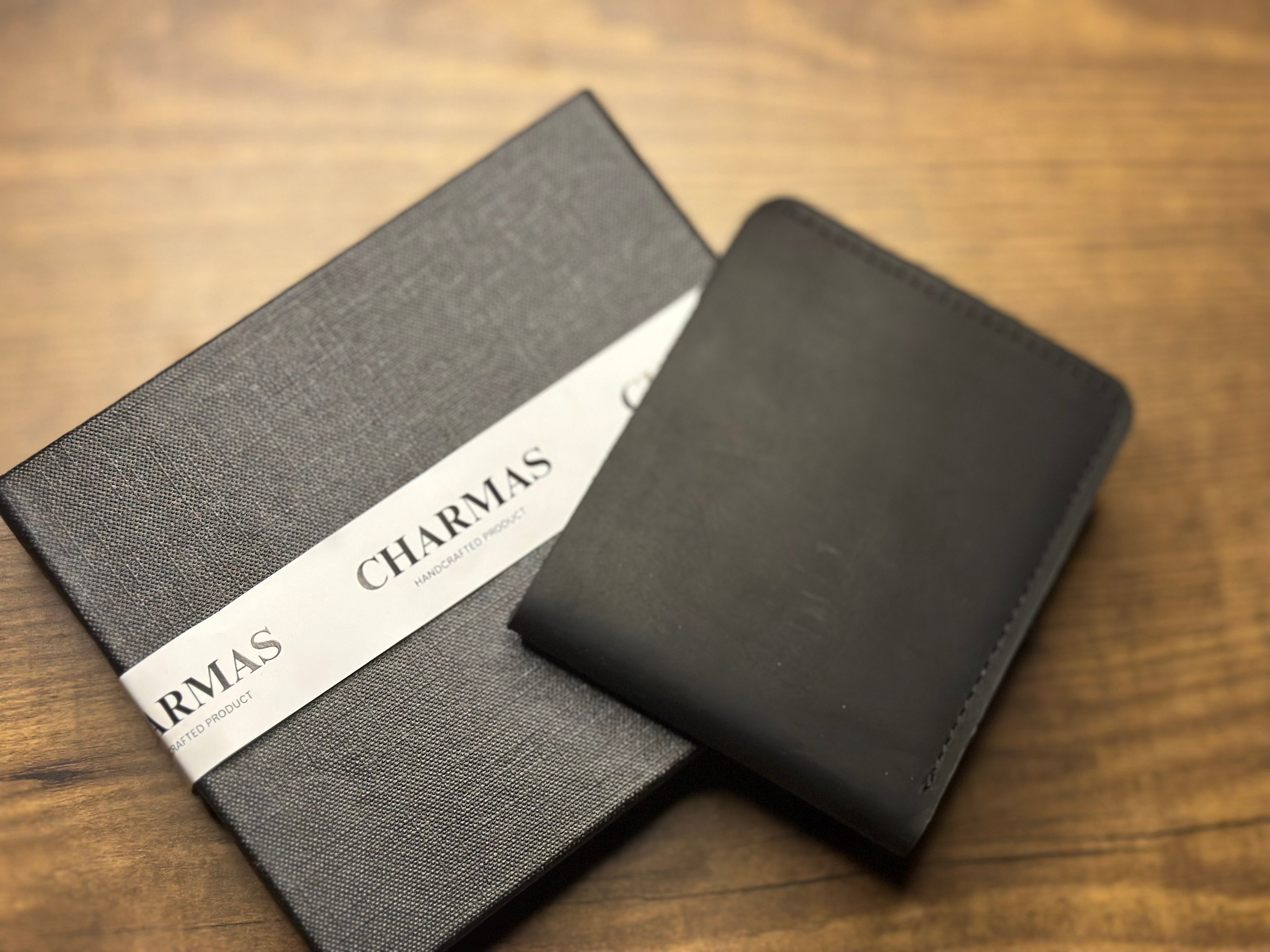 Black notebook and black wallet with 'CHARMAS' branding on a wooden surface