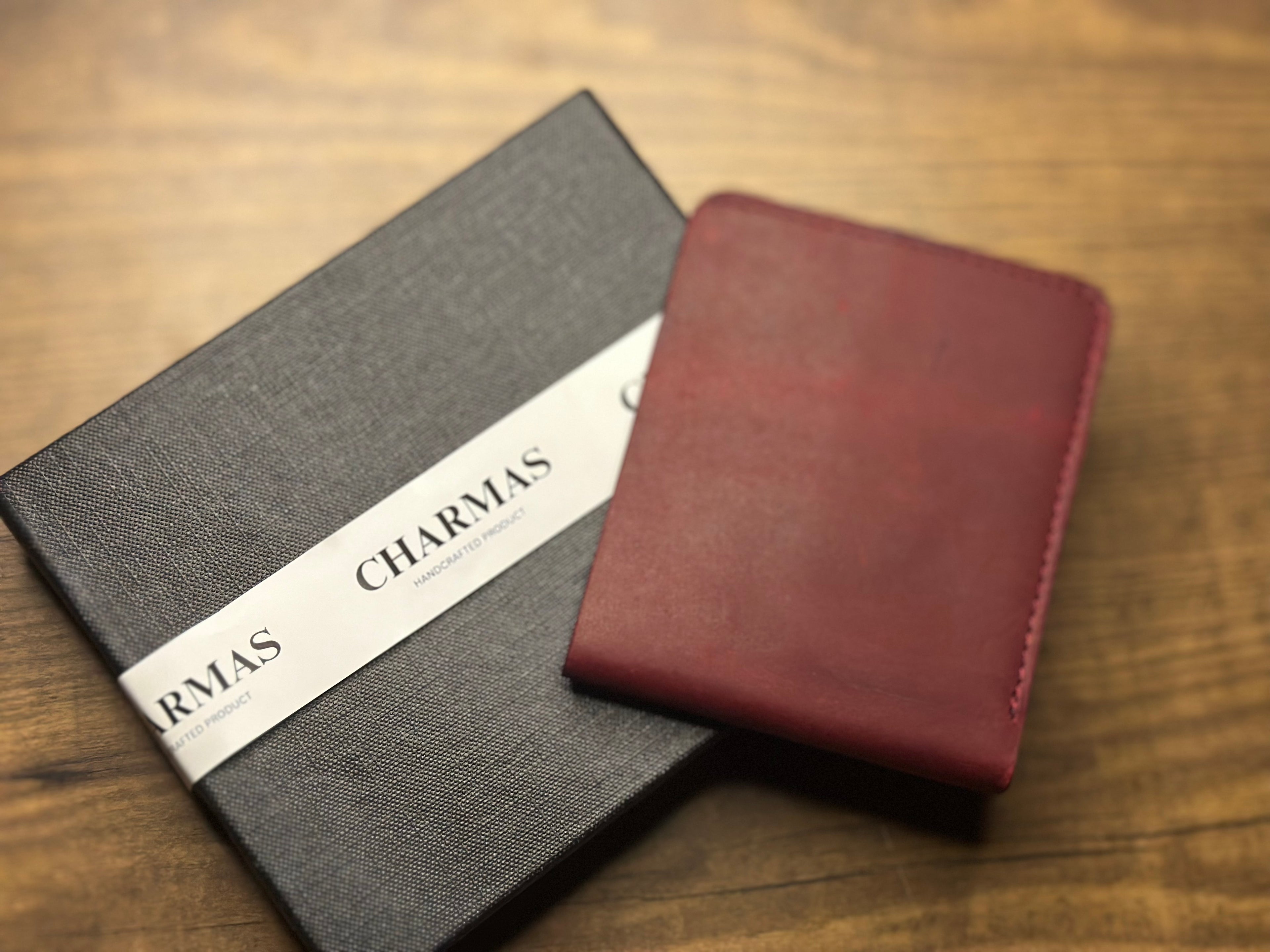 Gray notebook with 'CHARMAS' branding and a red leather cover on a wooden surface