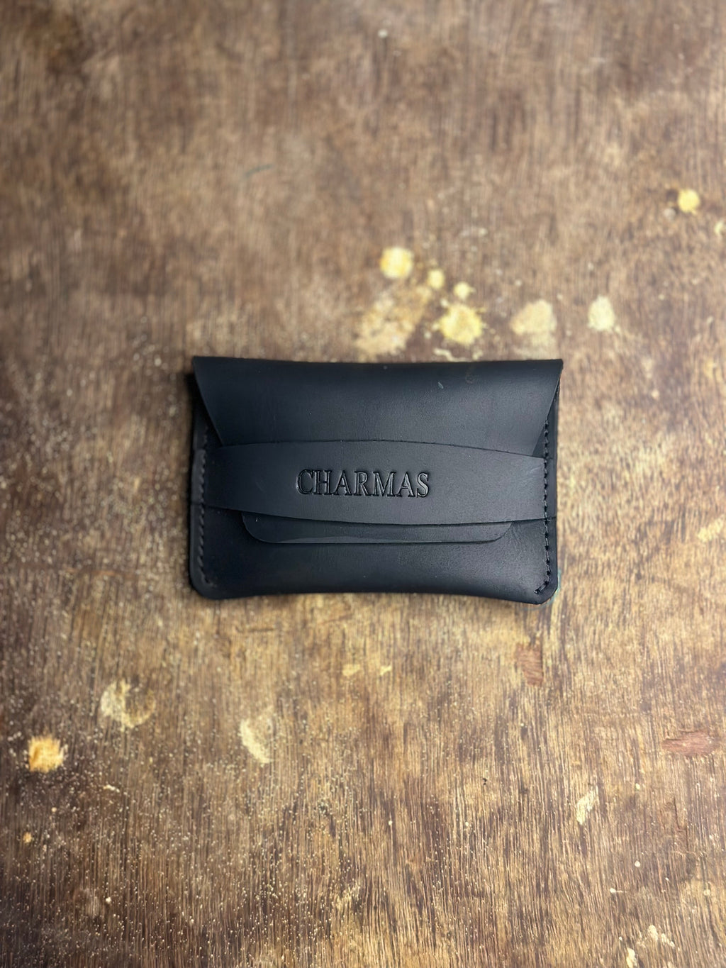 Black leather wallet with 'CHARMAS' branding on a textured brown surface